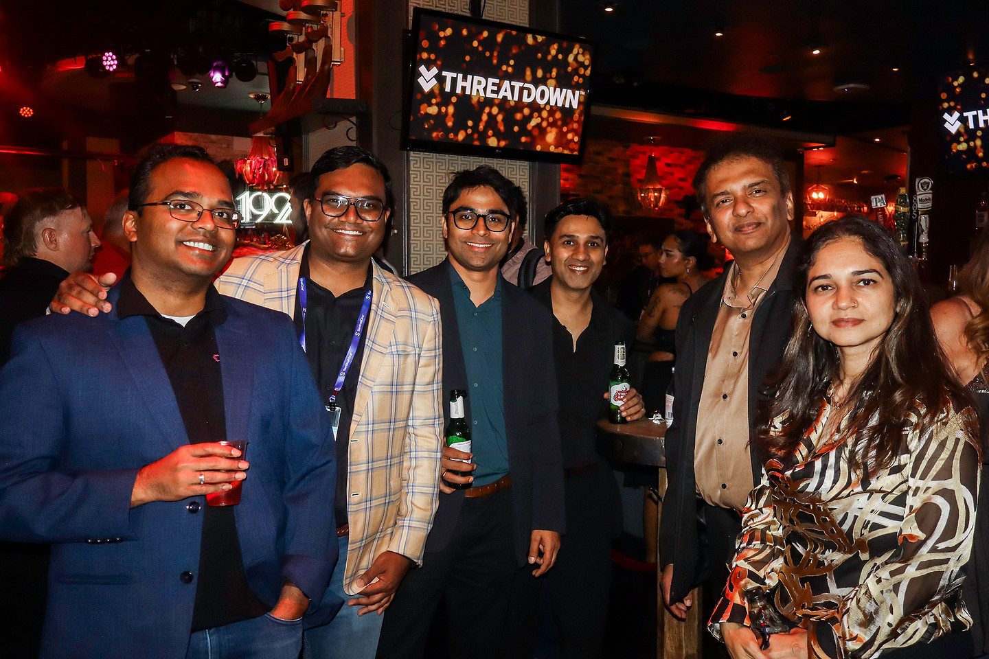 A group of guests with drinks in hand beneath the sponsor screens