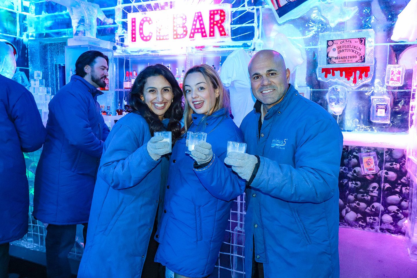 Three guests in parkas raising a toast beneath the ICEBAR sign