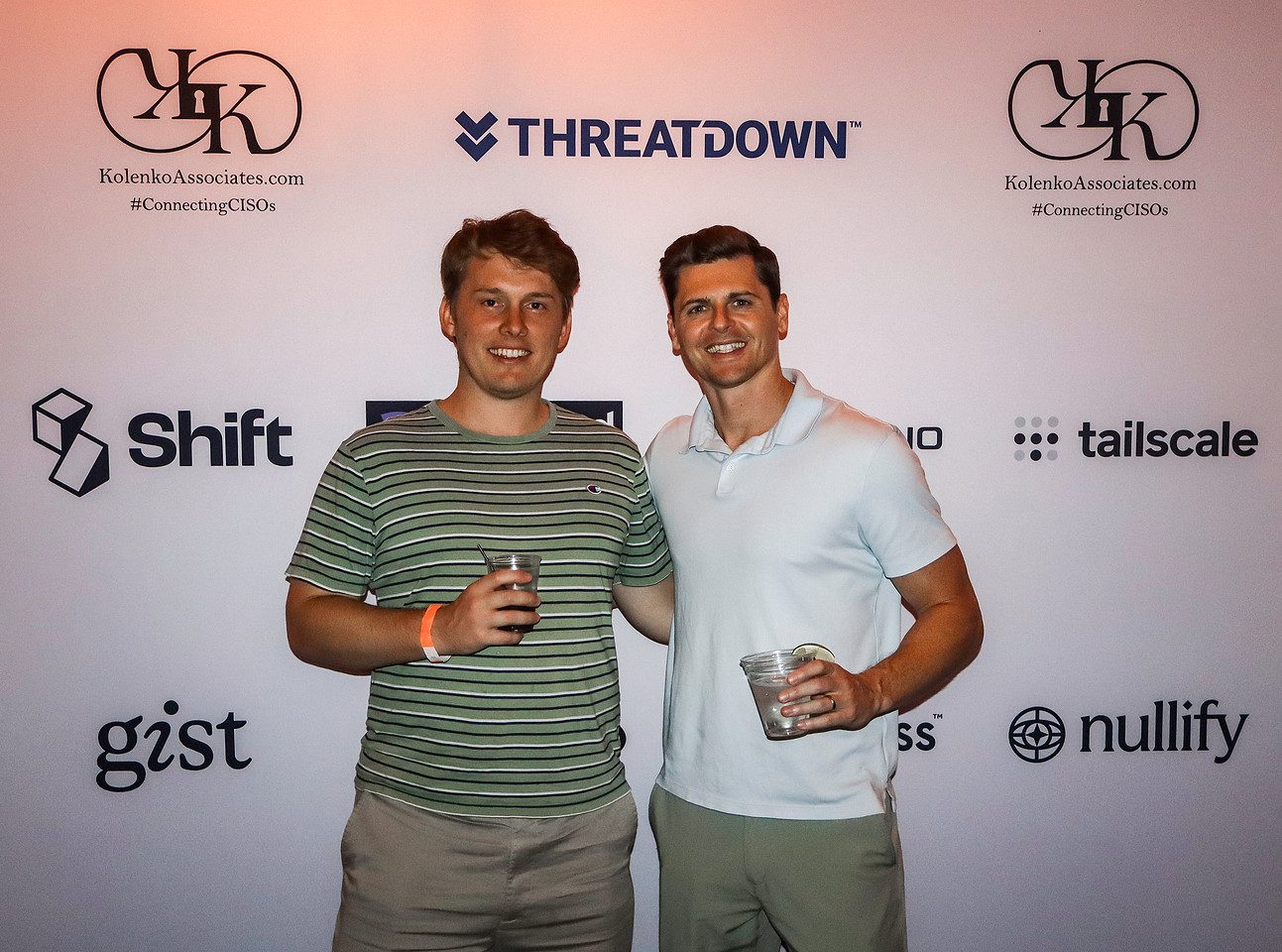 Two guests with drinks photographed at the sponsor backdrop