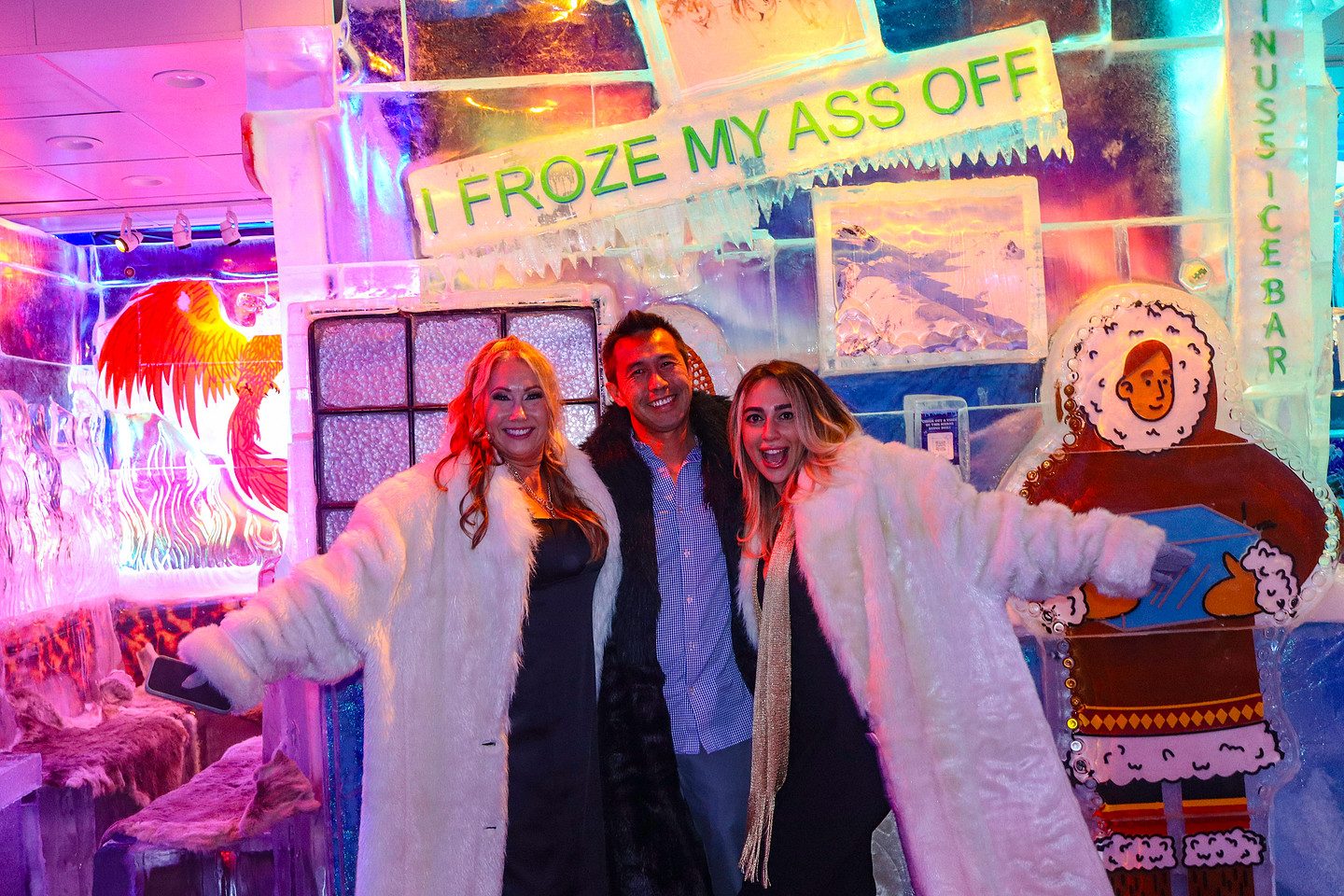 Three guests in fur coats beside a neon sign in the minus5 ICEBAR