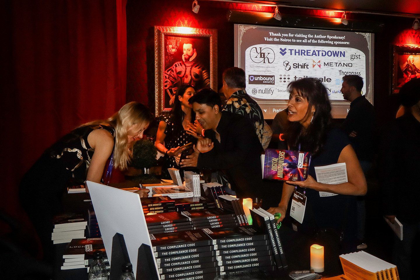 Guests signing books at the Author Speakeasy table, beneath a board thanking the evening&rsquo;s sponsors