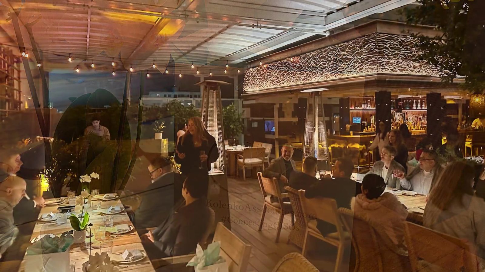 Guests at a Kolenko & Associates rooftop dinner at dusk, under festoon lights